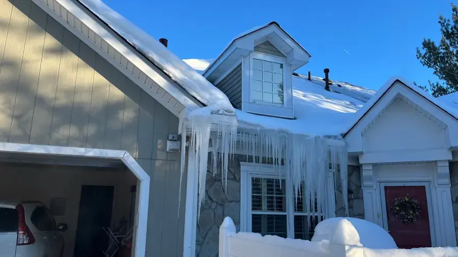 Ice dam and icicles along the eaves of a snow-covered Rochester, MI home