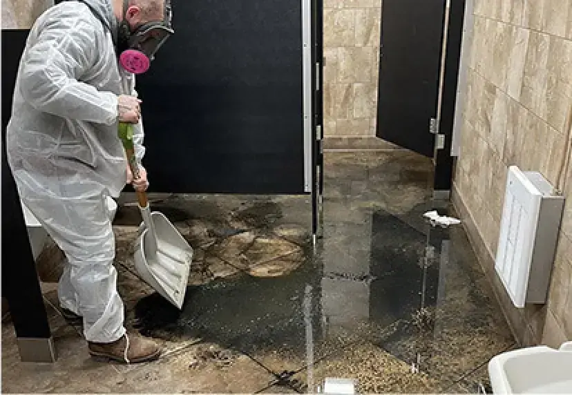 Technician in protective coveralls and respirator clearing sewage from a restroom floor in Rochester, MI